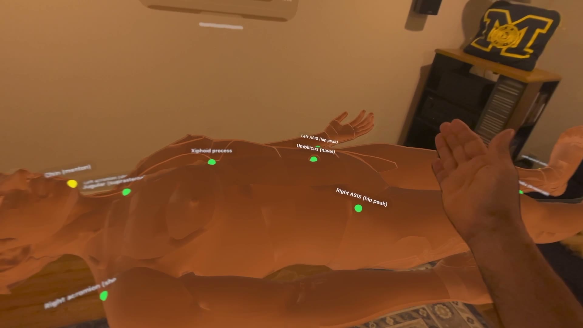 Headset view: a full-size anatomical patient lying in a room, with green landmark points labeled chin, jugular notch, xiphoid process and hip peaks